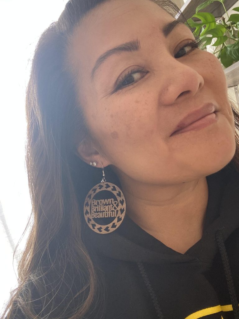 Tracie Noriega wearing earrings that say "Brown Brilliant & Beautiful"